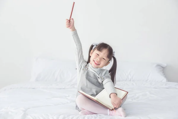 Девушка сидит на кровати и улыбается, держа карандаш — стоковое фото