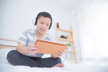 Yatak odasında tablet bilgisayar kullanırken kulaklık giyen çocuk