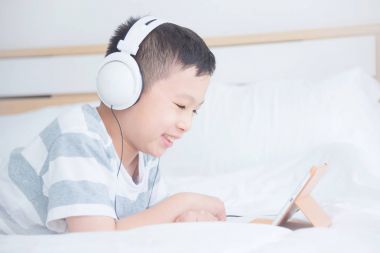 Yatak odasında tablet bilgisayar kullanırken kulaklık giyen çocuk