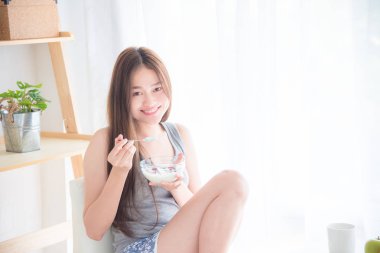 Yakın cam kenarında oturan ve yoğurt tutan güzel Asyalı kadın 