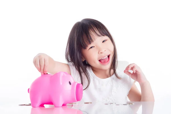 小亚洲女孩把硬币放在粉红色的小猪银行的白色背景 — 图库照片