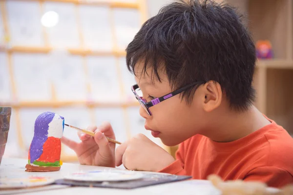 boy painting craft by color in classroom