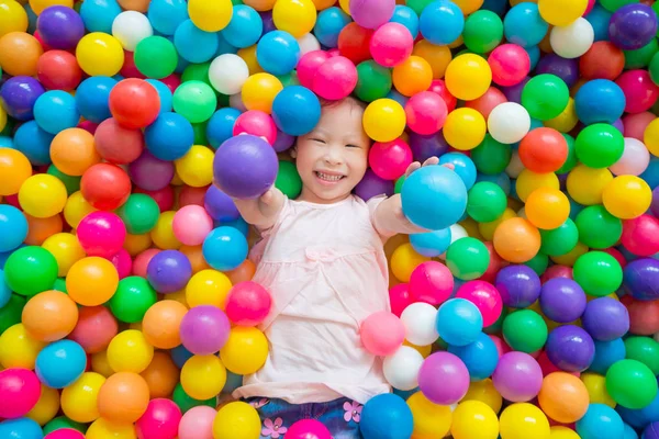 Chica sonriendo mientras está acostado en muchas bolas de color en el patio interior —  Fotos de Stock