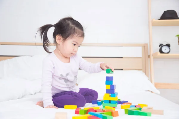 Dívka hraje barevné dřevěné kostky na posteli — Stock fotografie