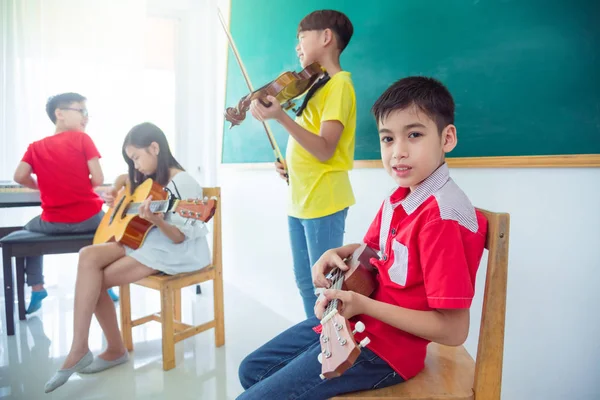 Young asian boy playing ukulele with friends in music classroom