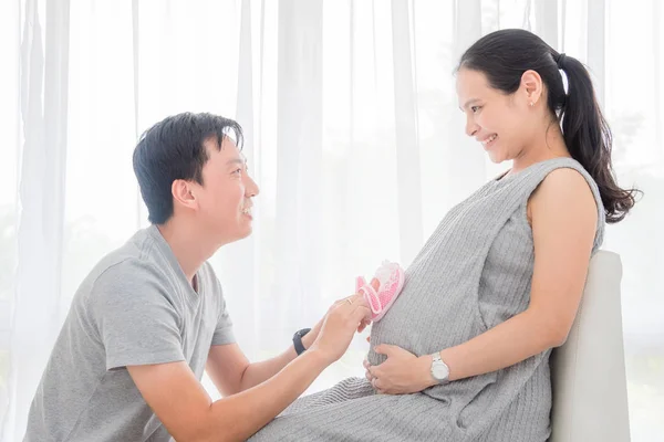 丈夫把小婴儿鞋放在他怀孕的妻子的肚子上 — 图库照片