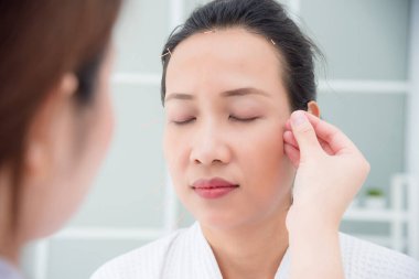Güzel Asyalı kadın klinikte yüz akupunktur tedavisi görüyor.