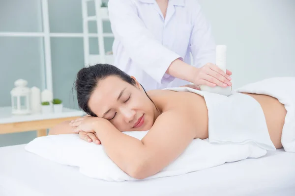 Krásná žena ležící na posteli a terapeut masáže herballem — Stock fotografie
