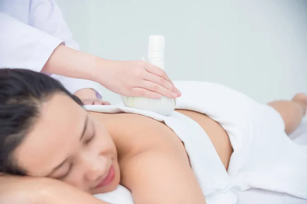 Mujer acostada en la cama y terapeuta masajeando con una bola de hierbas — Foto de Stock