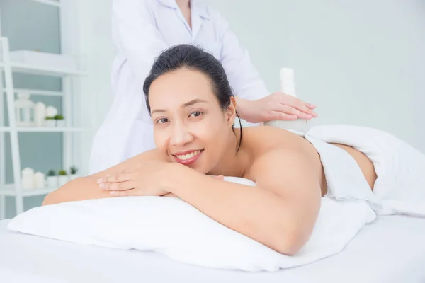 Mulher bonita sorrindo enquanto terapeuta massageando por bola de ervas — Fotografia de Stock