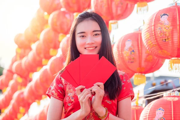 Piękna azjatycka kobieta w tradycyjnej chińskiej długiej sukience trzyma czerwoną kopertę i uśmiecha się — Zdjęcie stockowe