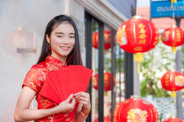 Beautiful asian woman in traditional chinese long dress holding red envelope and smiles