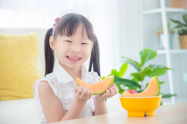 Little girl holding a slice of japanese melon and smiles — Stock Photo, Image