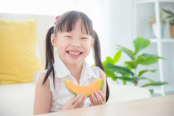 Little girl holding a slice of japanese melon and smiles — Stock Photo, Image