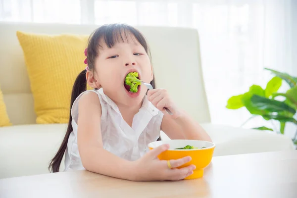 Little asian girl eating broccoli at home. — Stock Photo, Image