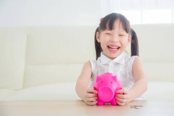 Маленькая азиатская девочка держит розовую копилку и улыбается . — стоковое фото