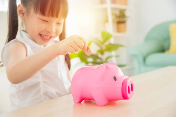 Niña inserta moneda en la alcancía rosa y sonríe . —  Fotos de Stock