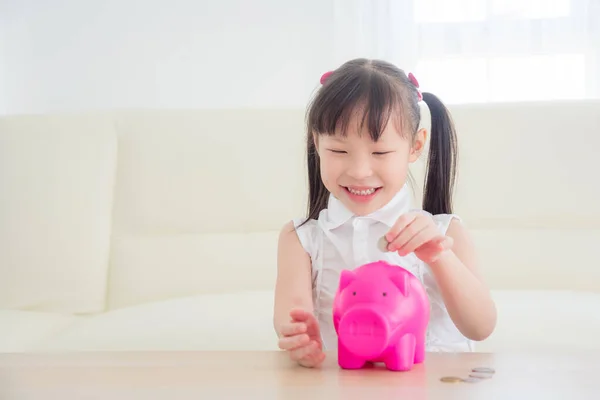 亚洲小女孩把硬币放进粉红的储蓄罐里 — 图库照片
