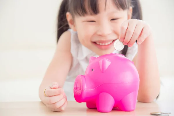 Маленькая девочка вставляет монетку в розовую копилку и улыбается. . — стоковое фото
