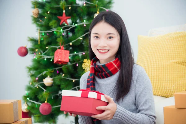 Mooi jong aziatisch meisje zitten op de vloer in de woonkamer en het houden van geschenkdoos en glimlacht — Stockfoto