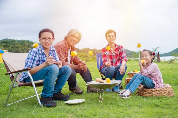 Group of asian family grilling sweet corn on stove at camping site