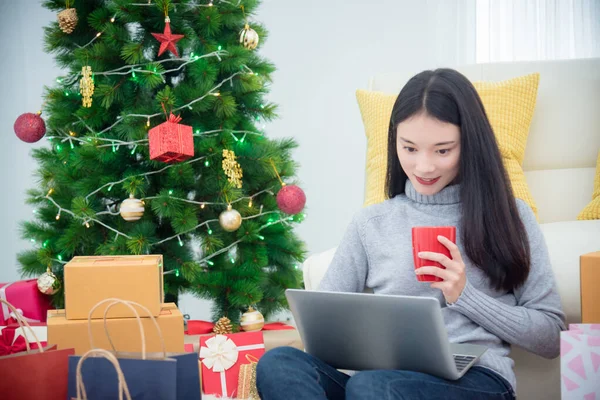 Mooi jong aziatisch meisje zitten op de vloer in de woonkamer en met behulp van notebook computer voor winkelen Stockfoto