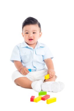 Küçük erkek çocuk yerde oturuyor ve tahta bloklarla oynuyor.