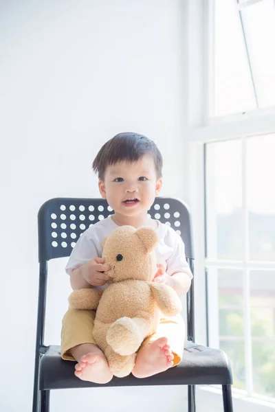 Kleine jongen zit op stoel met zijn teddybeer en glimlacht — Stockfoto