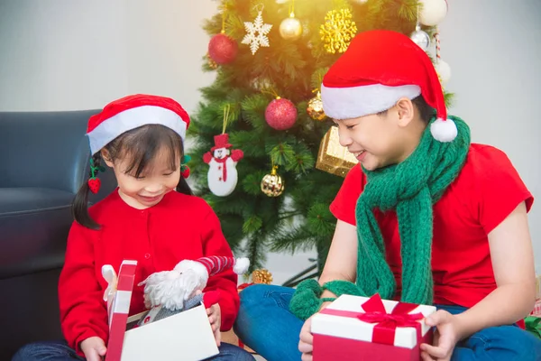 Klein Aziatisch meisje en haar broer zitten op de vloer en openen geschenkdoos met glimlach — Stockfoto