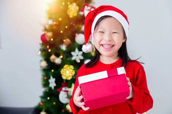 Klein aziatisch meisje draagt kerstman hoed en houden geschenkdoos met glimlach — Stockfoto