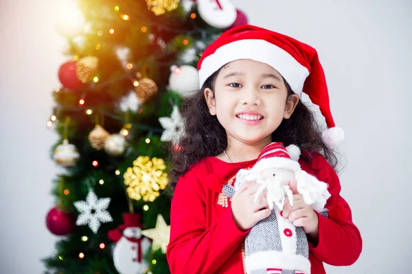 Klein aziatisch meisje dragen santa claus hoed en houden pop met glimlach — Stockfoto