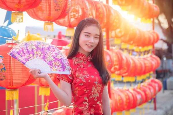 Beautiful asian girl in chinese traditional costume holding fan in front of red chinese lantern.