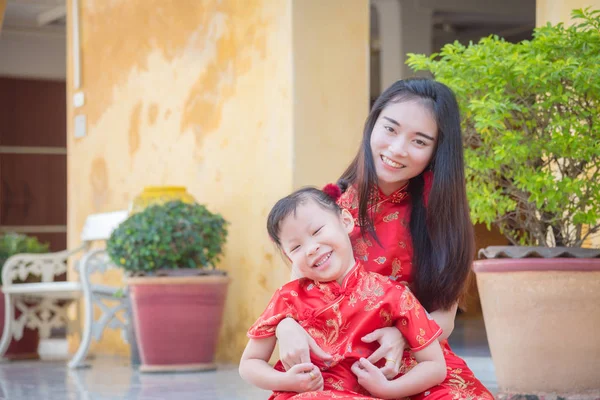 Menina e sua mãe em traje tradicional chinês sentado na frente de sua casa e sorrindo alegremente . — Fotografia de Stock