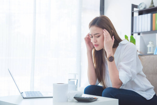 Young asian beautiful woman having headache sitting on sofa.
