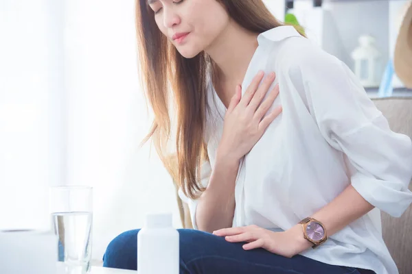 Mujer joven que tiene dolor en el pecho mientras está sentada en el sofá . — Foto de Stock