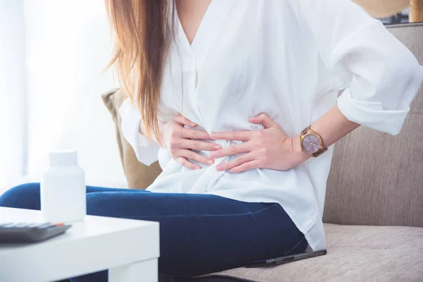 Una mujer con dolor de estómago sentada en el sofá y sosteniendo su vientre . —  Fotos de Stock