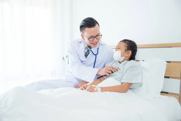 若いアジア系男性の医者は病院病棟のベッドで子供の患者を訪ねた 聴診器で患者の肺の音を聞く医師 — ストック写真