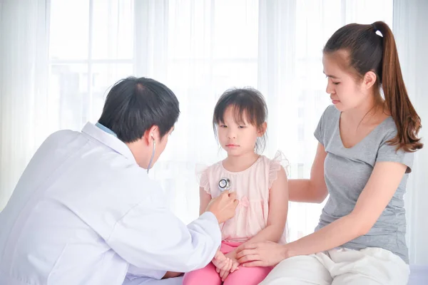 亚洲医生在医院用听诊器检查女孩的身体 女孩的母亲坐在女儿旁边 — 图库照片