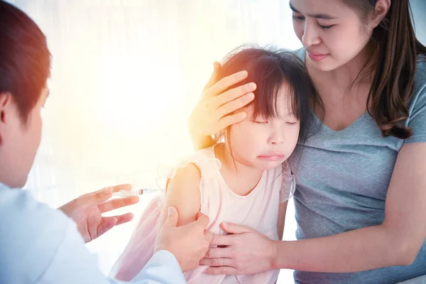 亚洲医生为一名在医院的女孩和坐在女儿旁边的女孩的母亲注射疫苗 — 图库照片