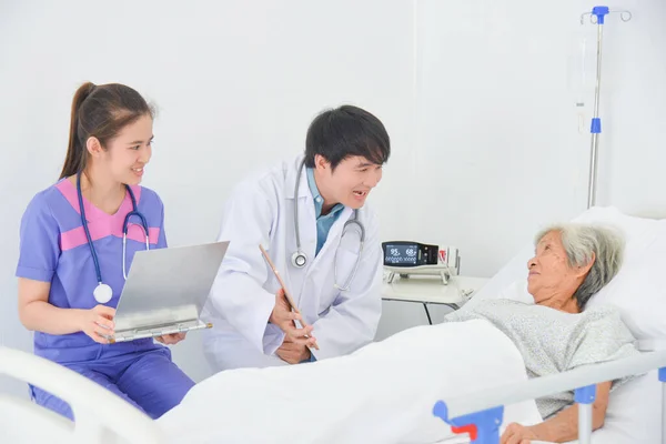 医師はアジアの高齢女性への病気の症状や予防策を説明します 患者は病棟のベッドに横たわっています — ストック写真
