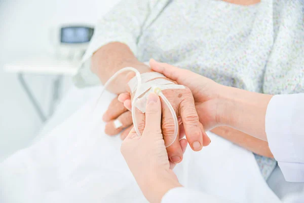 病院のベッドに横になっている高齢者の手を握っている医師の手 — ストック写真