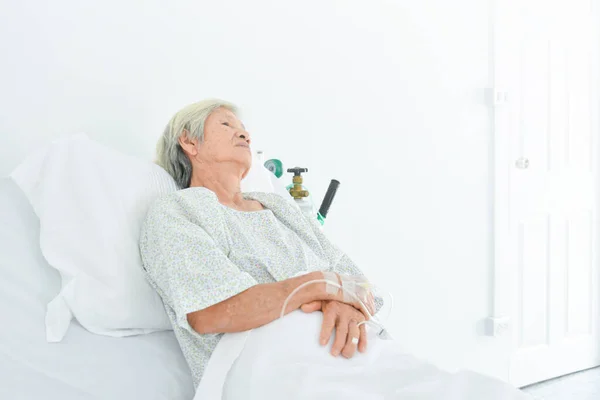 病院病棟のベッドの上に寝そべって窓の外を見ている孤独なアジアの高齢女性患者が彼女の家族が訪れるのを待っている — ストック写真