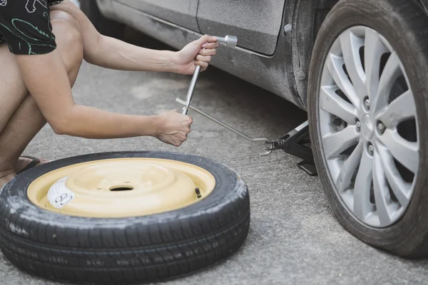 Mujer cambiando de rueda en una carretera — Foto de Stock