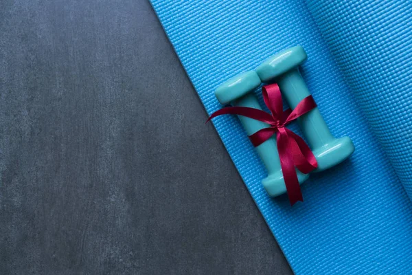 two green dumbbell with red gift bow on blue yoga mat background