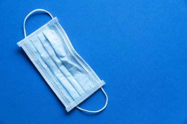 Tıbbi tek kullanımlık yüz maskesi mavi masa arkaplanındaki kovid-19 veya koronavirüsten korur. Sağlıklı ve ilaç konsepti.