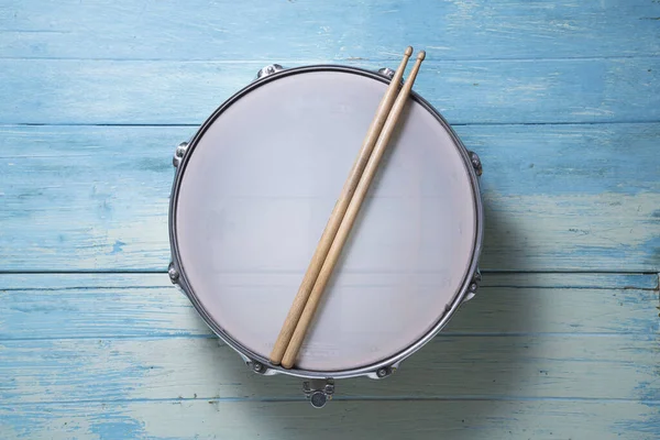 Drum stick and drum on the blue table background, top view, music concept