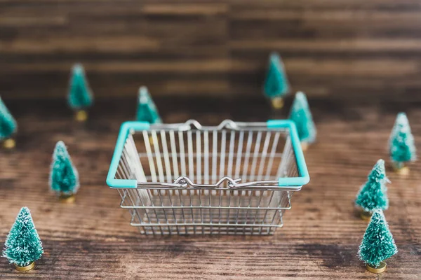 Koszyk zakupów otoczony miniaturowymi choinkami — Zdjęcie stockowe