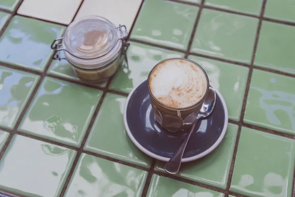 Café con leche de soja en taza oscura en la mesa de azulejos verdes junto al azúcar — Foto de Stock