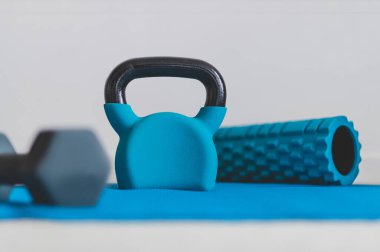 Ev jimnastik salonu ve spor salonu konsepti, kettlebell köpük silindirli mavi yoga minderi ve düşük perspektiften sığ alan derinliğinde dambıl atışı.