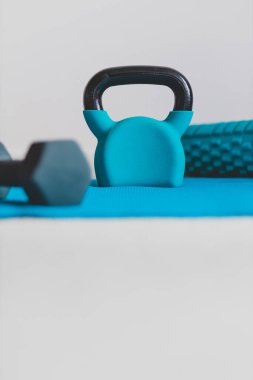 Ev jimnastik salonu ve spor salonu konsepti, kettlebell köpük silindirli mavi yoga minderi ve düşük perspektiften sığ alan derinliğinde dambıl atışı.
